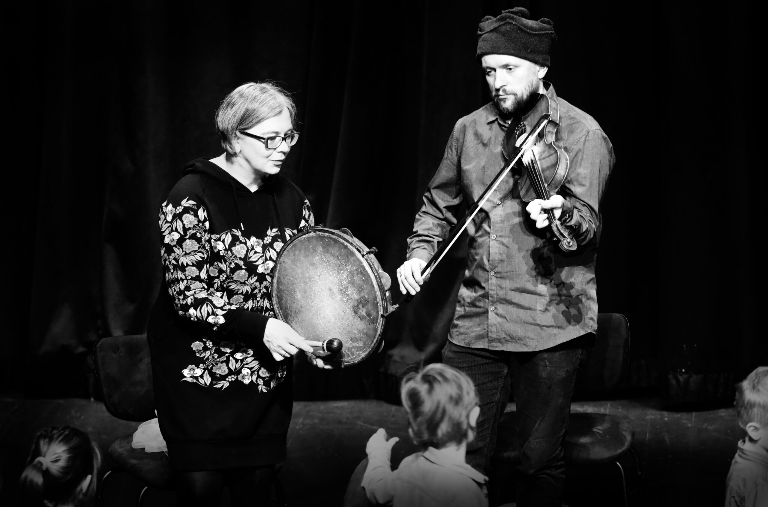 Czarno-biała fotografia kobiety i mężczyzny, którzy grają na bębenku i skrzypcach.